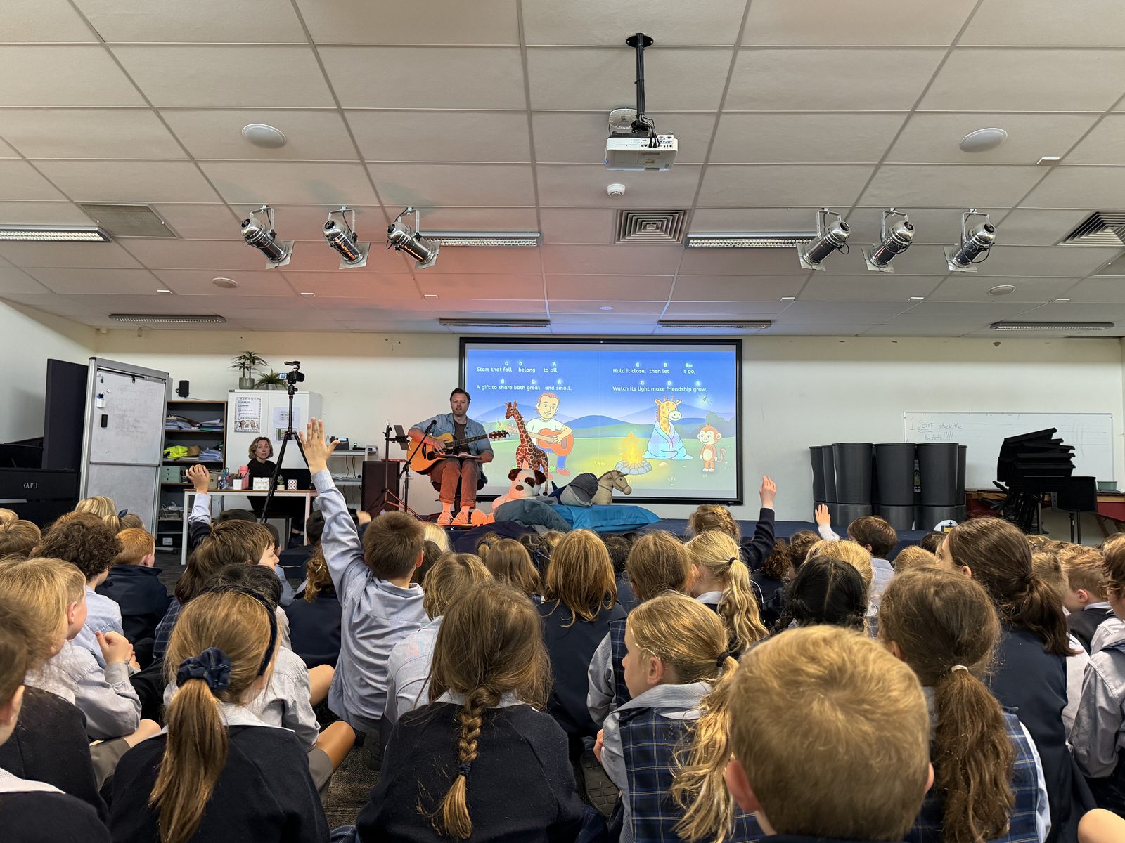 Children seen from behind raising their hands during Mr H's school show