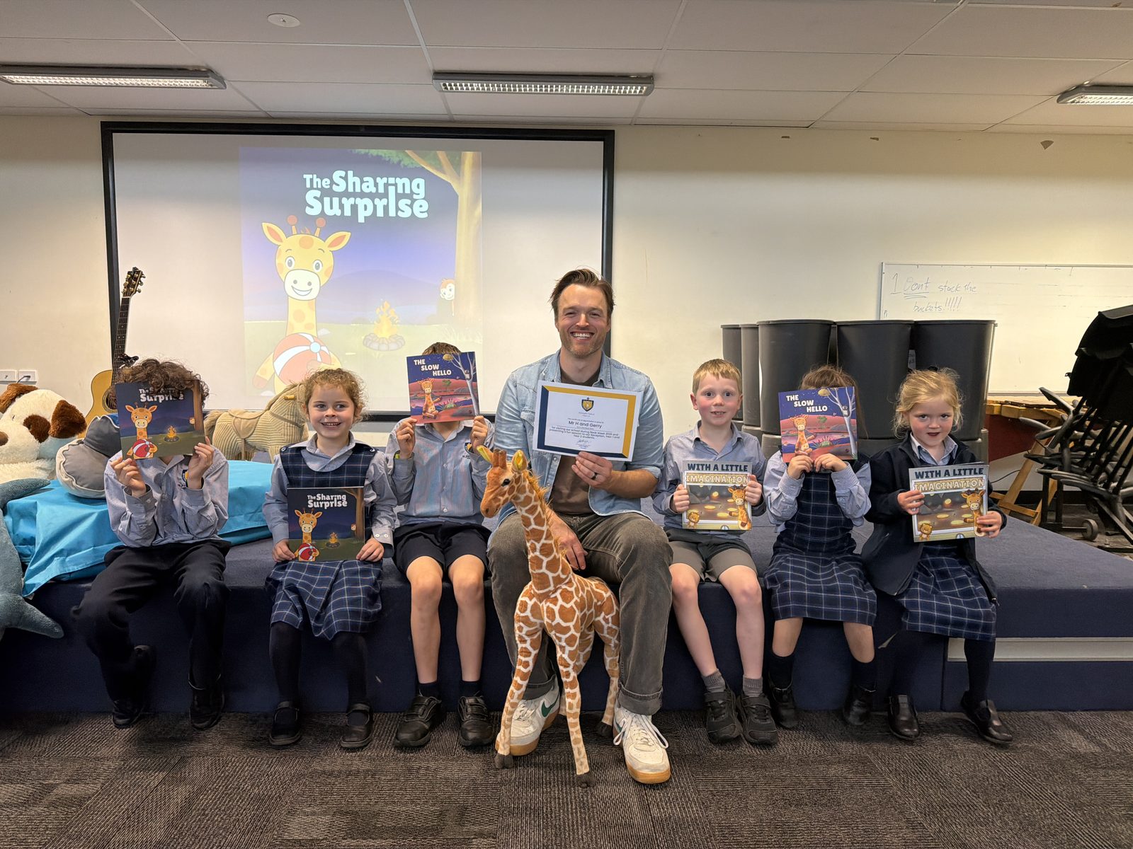 Mr H seated with his school certificate, Gerry and students holding their One More Story books